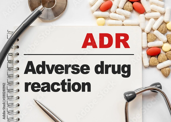 Fototapeta Page in notebook with ADR Adverse drug reaction on white background with stethoscope and group of pill. Medical concept. Term and abbreviation