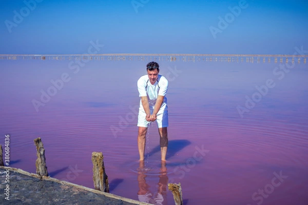 Obraz Brunet man relaxing on pink salty Sivash Lake near Azov Sea, colored by microalgae Dunaliella salina, enriching water of the lake by beta-carotene
