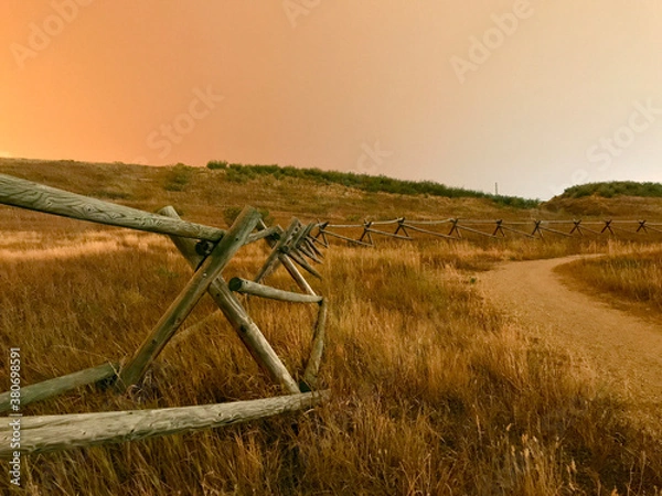 Obraz California, Oregon, Colorado wildfire orange smokey sky above rustic split log fence