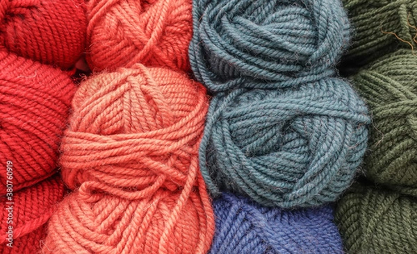 Obraz Colorful woolen balls of yarn. Background of colored yarn balls. Needlework. Knitting. Hobbies and leisure. Balls of yarn in red, orange, grey, blue and green colors.