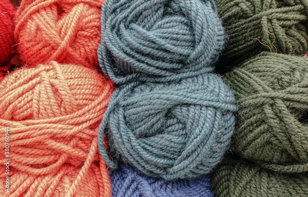 Obraz Colorful woolen balls of yarn. Background of colored yarn balls. Needlework. Knitting. Hobbies and leisure. Balls of yarn in orange, grey, green colors.