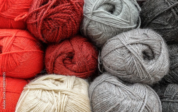Obraz Colorful woolen balls of yarn. Background of colored yarn balls. Needlework. Knitting. Hobbies and leisure. Balls of yarn in shades of orange, red, grey, dark grey and seashell colors.