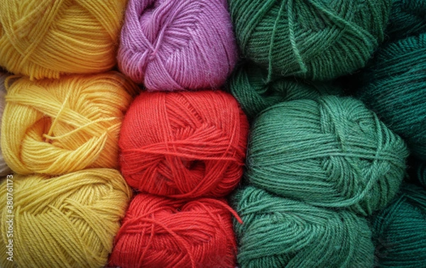 Obraz Colorful woolen balls of yarn. Background of colored yarn balls. Needlework. Knitting. Hobby and leisure. Balls of yarn in yellow, red, green and orchid colors.