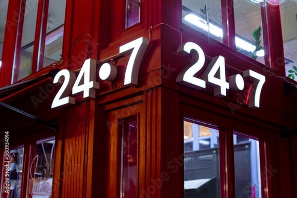 Fototapeta red store on the corner with a luminous sign 24/7, English style red store with glass windows, a night scene of building facade lighting details.