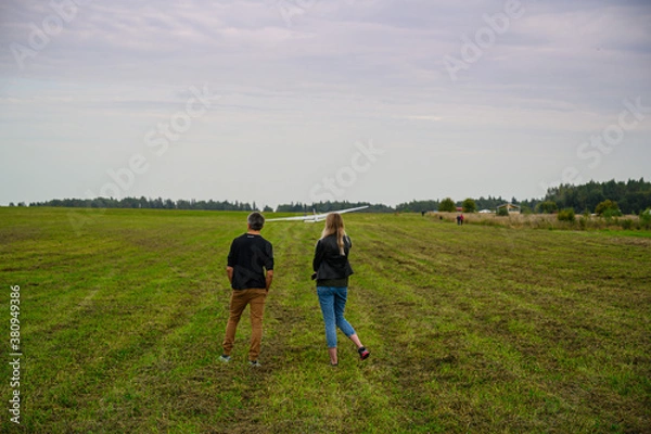 Obraz a man and a woman stand on a green field and look at a landed glider 