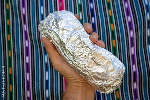 Fototapeta Large Whole California-style Burrito Wrapped in Foil being held in a Hand