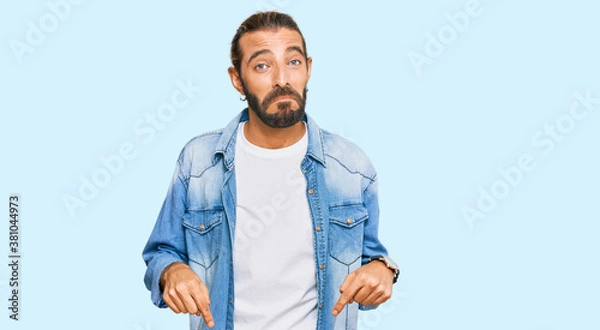 Fototapeta Attractive man with long hair and beard wearing casual denim jacket pointing down looking sad and upset, indicating direction with fingers, unhappy and depressed.