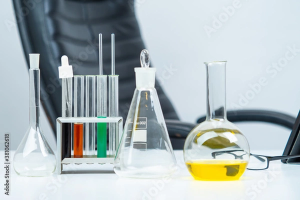 Fototapeta Transparent test tubes on background of empty chair. Laboratory glass on table. Concept - use of laboratory glass by chemist. Laboratory glass for sale. Equipment for lab. Labware of various shapes.