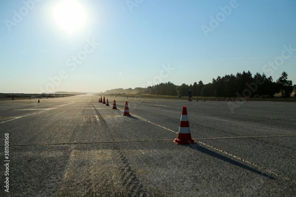 Fototapeta Several traffic cones standing in the line on the ground of the old airfield. Prepared for the testing of the cars. 