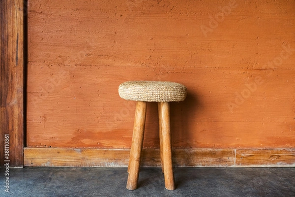 Fototapeta Handmade wooden chair with wicker straw pillow on background of red terracotta wall with decorative plaster. Moroccan rustic interior and furniture design.