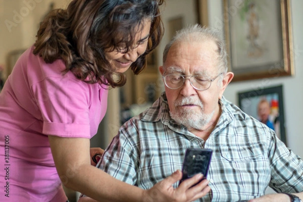 Obraz Smiling senior man and caregiver with smartphone are doing a videocall