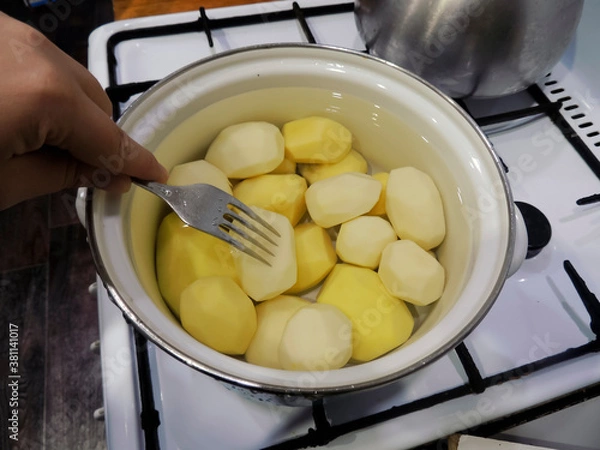 Fototapeta Raw potatoes are cooked in water. Cooking potatoes in a pot. Test readiness with a metal fork.
