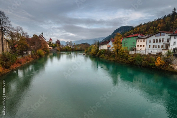 Fototapeta Wonderful landscape of mountain village in fall. View of forest with yellowed foliage, which reflects in water. Fussen. Lech river. Bavaria. Germany.