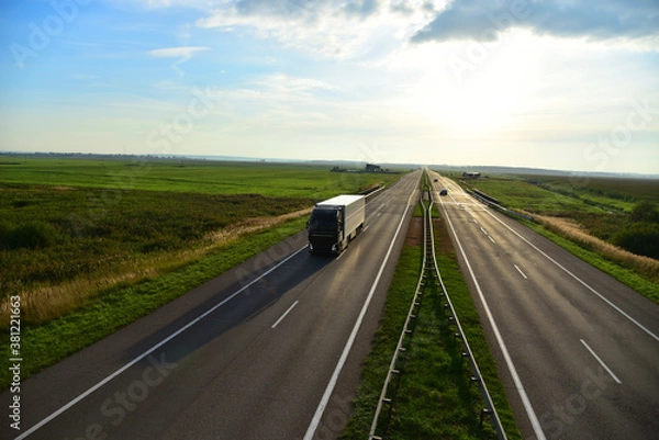 Fototapeta Truck with semi-trailer driving along highway on the sunset background. Goods delivery by roads. Services and Transport logistics. soft focus. Object in motion.