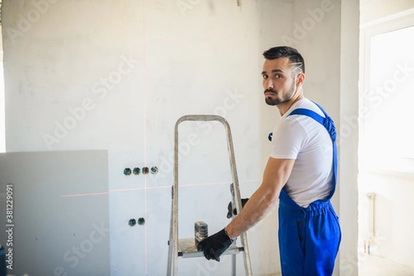 Fototapeta A handyman moves an aluminum step ladder around the room