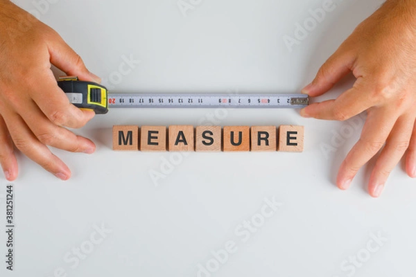 Fototapeta Building concept with wooden cubes on white background flat lay. hands holding extented measuring tape.