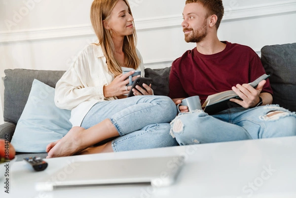 Obraz Image of ginger happy couple using cellphone and reading book