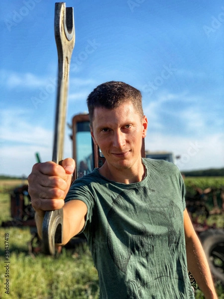 Obraz Young smiling handsome worker with wrench outdoor near tractor