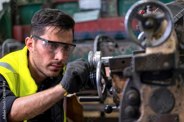 Fototapeta Engineer or supervisor wearing safety glass and glove, concentrate on adjusting the gap of the milling (lathe) machine at the iron manufacturing factory. Heavy sweating on his face. Industrial area..
