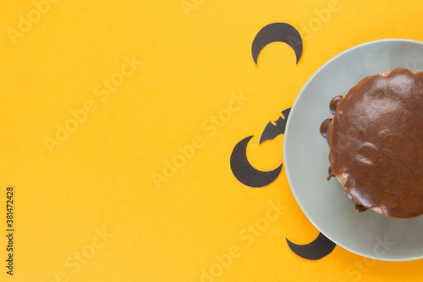 Obraz Halloween concept, trick or treat. Bat and moon peeps from under a plate with chocolate cake. Orange background, handmade cooking. Copy space, flat lay. Selective focus, blur.