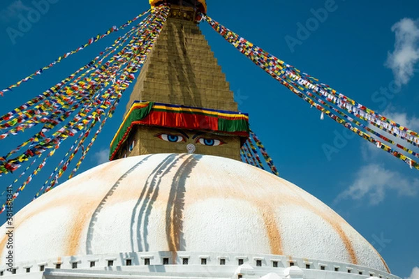Fototapeta The upper part of the Boudhanath stupa in Kathmandu, Nepal. The image of Buddhas eyes on a gold surface of the stupa. Colorful prayer flags nearby.