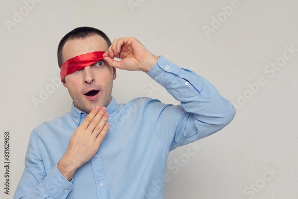 Fototapeta Excited and dazed man removes red blindfold, portrait, white background, copy space