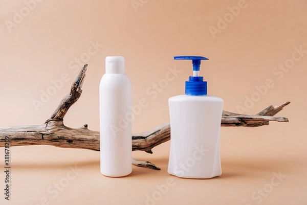 Obraz White bottles and a dry tree branch on a beige background.