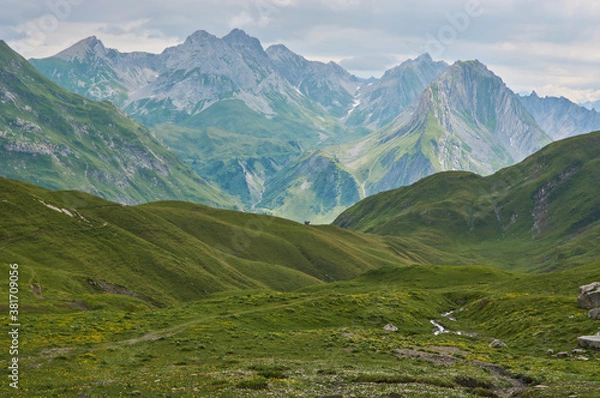 Fototapeta Beautiful lonely mountain landscape in the alps. Panoramic mountain landscape in the alps with green meadows and high mountains in the distance. Remote place in the mountains.