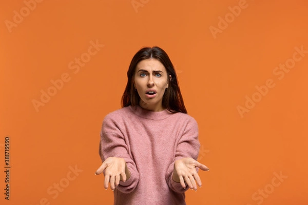 Fototapeta Why. whats next. Portrait of Indignant shocked beautiful woman in pink sweater keeps palm raised, cant understand something, isolated on orange background