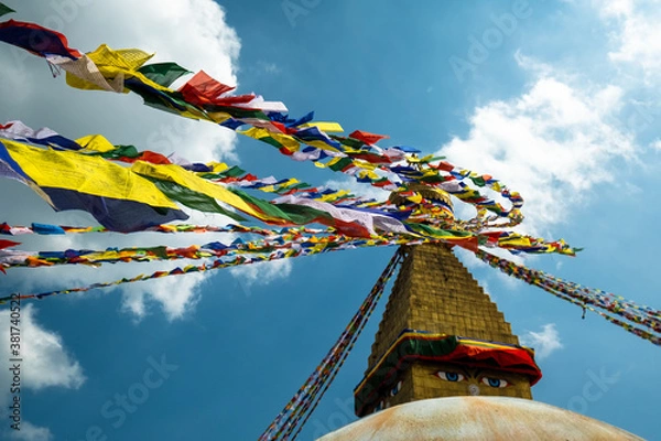 Fototapeta Multicolored Buddhist prayer flags with mantras on a background of blue sky and an ancient stupa. Traditional Tibetan and Nepalese threads with rectangular colored pieces of fabric.
