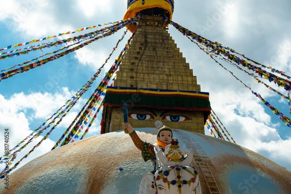 Fototapeta The upper part of the Boudhanath stupa in Kathmandu, Nepal. The image of Buddhas eyes on a gold surface of the stupa. Colorful prayer flags nearby. Buddha statue on a white elephant.