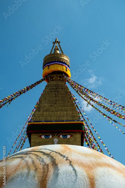 Fototapeta The upper part of the Boudhanath stupa in Kathmandu, Nepal. The image of Buddhas eyes on a gold surface of the stupa. Colorful prayer flags nearby.