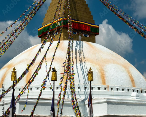Fototapeta The upper part of the Boudhanath stupa in Kathmandu, Nepal. The image of Buddhas eyes on a gold surface of the stupa. Colorful prayer flags nearby