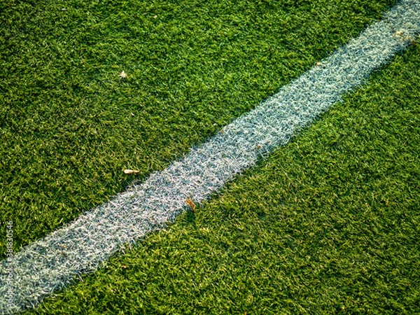 Fototapeta Close up image of white lines of kick-off circle on a football field with synthetic turf. White layout of the center circle on soccer field with green synthetic grass lawn with warm autumn sun light.