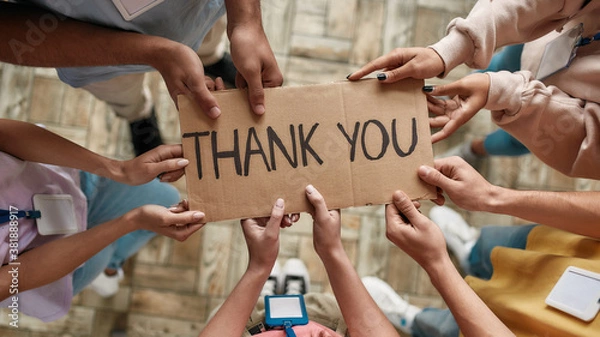 Obraz Top view of diverse young volunteers holding card with Thank you lettering while standing in charitable organization office