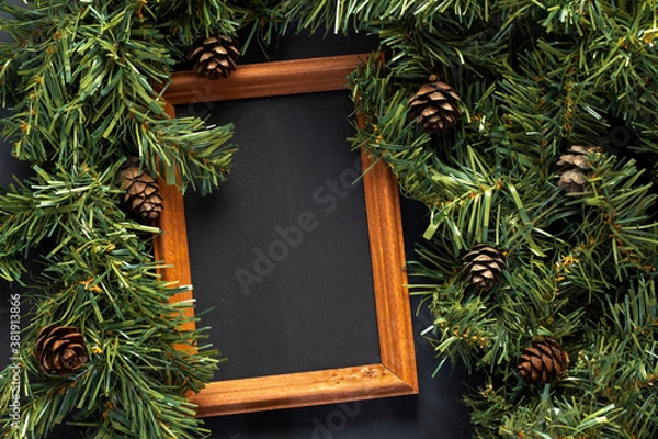 Obraz A wooden board for drawing with chalk lies near the Christmas tree branches with cones.
