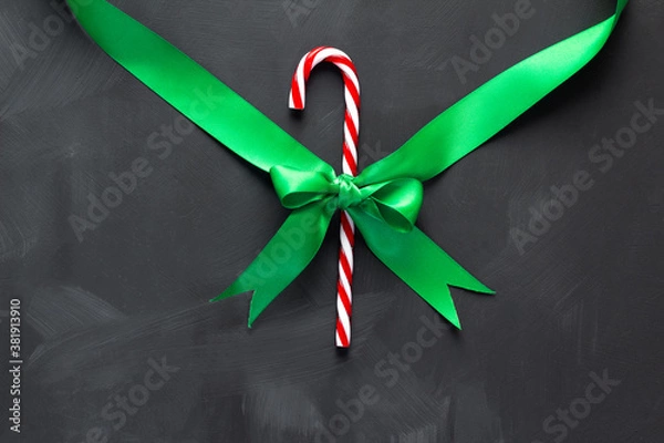 Fototapeta Candy cane tied with a green ribbon on a dark background.