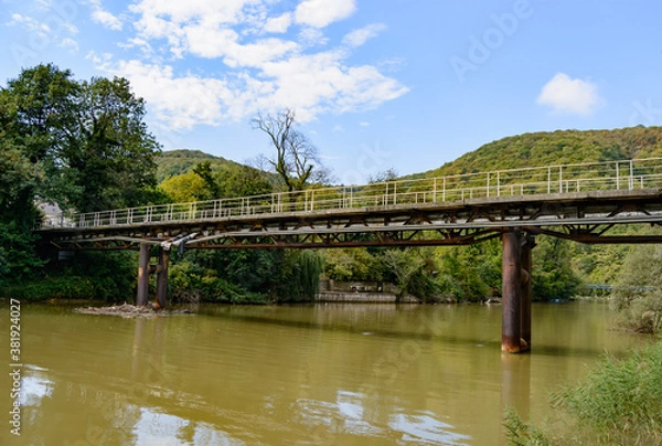 Fototapeta Beautiful mountain range with a bridge over the river in summer against a blue sky with clouds. blurry focus