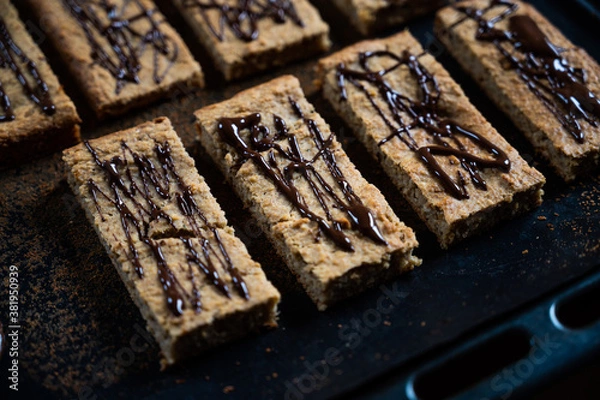 Fototapeta homemade protein müsli bar with banana and oatmeal decorated with dark chocolate as a healthy alternative without sugar, presented on the baking tray, moody photography style