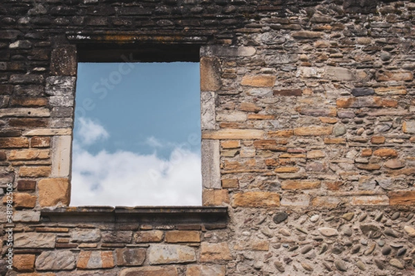 Obraz Window in ancient stone wall of damaged house, toned. Abandoned medieval building, filtered. Blue sky in window of ruin temple. Destroyed facade of old stone building. History concept. 