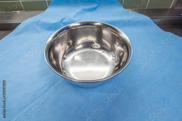 Fototapeta large silver saline bowl is wrapped in a blue paper towel in an operating room