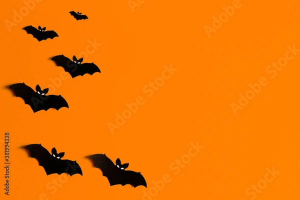 Obraz orange background with a flock of black paper bats for Halloween, black paper bat silhouettes on an orange background, Halloween concept, copyspace, flatlay, top view, overhead