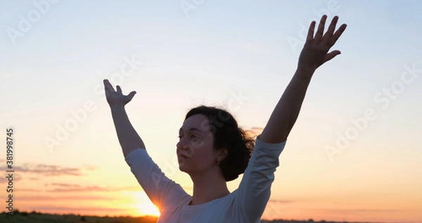 Fototapeta Female practicing qigong in summer fields with beautiful sunset on background	