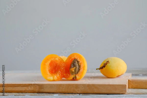 Fototapeta Apricots with cutting board on wooden and white gradient background, side view.