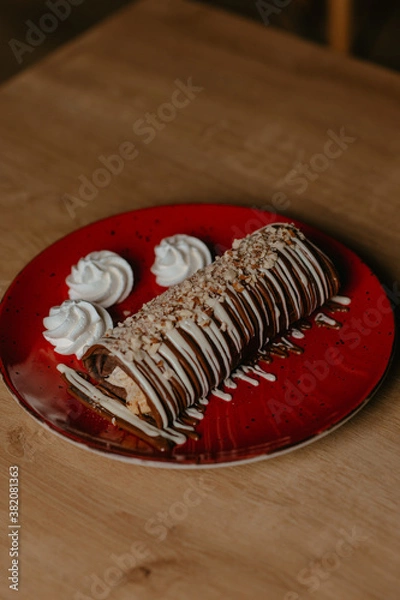 Fototapeta chocolate pancake with bananas, nuts and chocolate sauce. the toning. selective focus. a rolled chocolate pancake is a calorie bomb