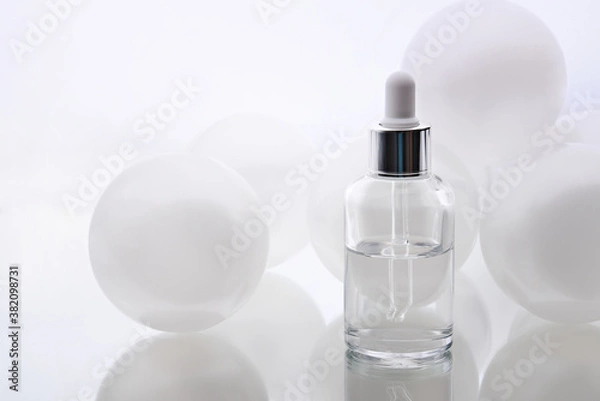 Fototapeta Cosmetic serum. Eyedropper with a drop and a bottle on a white mirror surface.