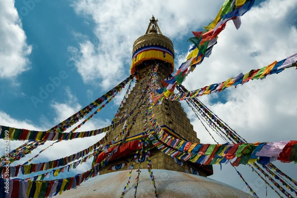 Fototapeta The upper part of the Boudhanath stupa in Kathmandu, Nepal. The image of Buddhas eyes on a gold surface of the stupa. Colorful prayer flags nearby.