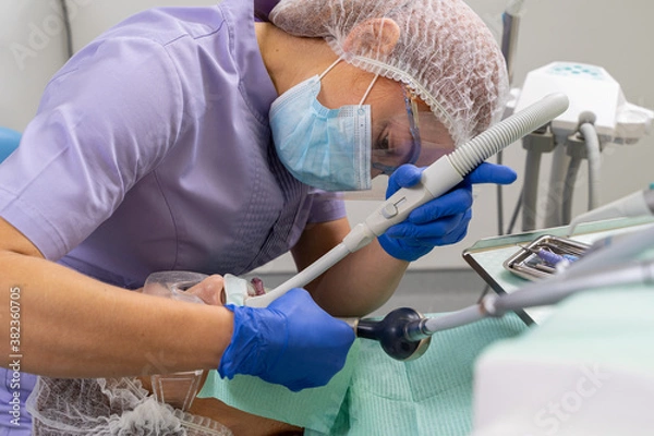 Fototapeta The dentist in an inconvenient position with the help of specialized instruments treats the patient's oral cavity.