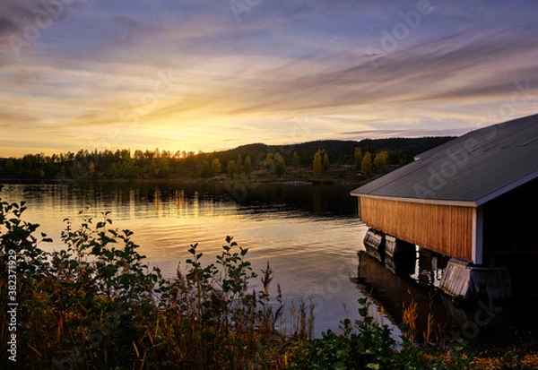 Obraz a red boathouse by the sea with sunset in the background