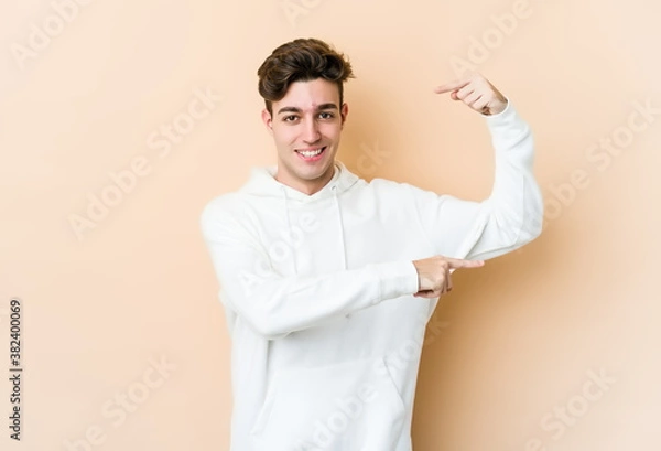 Fototapeta Young caucasian man isolated on beige background holding something little with forefingers, smiling and confident.